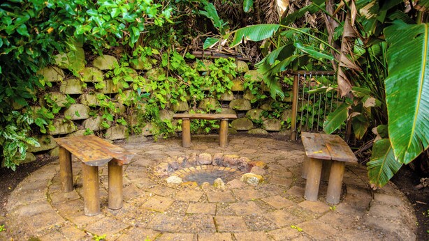 Un hogar de piedra con bancos, rodeado por un muro de piedra y abundante vegetación.