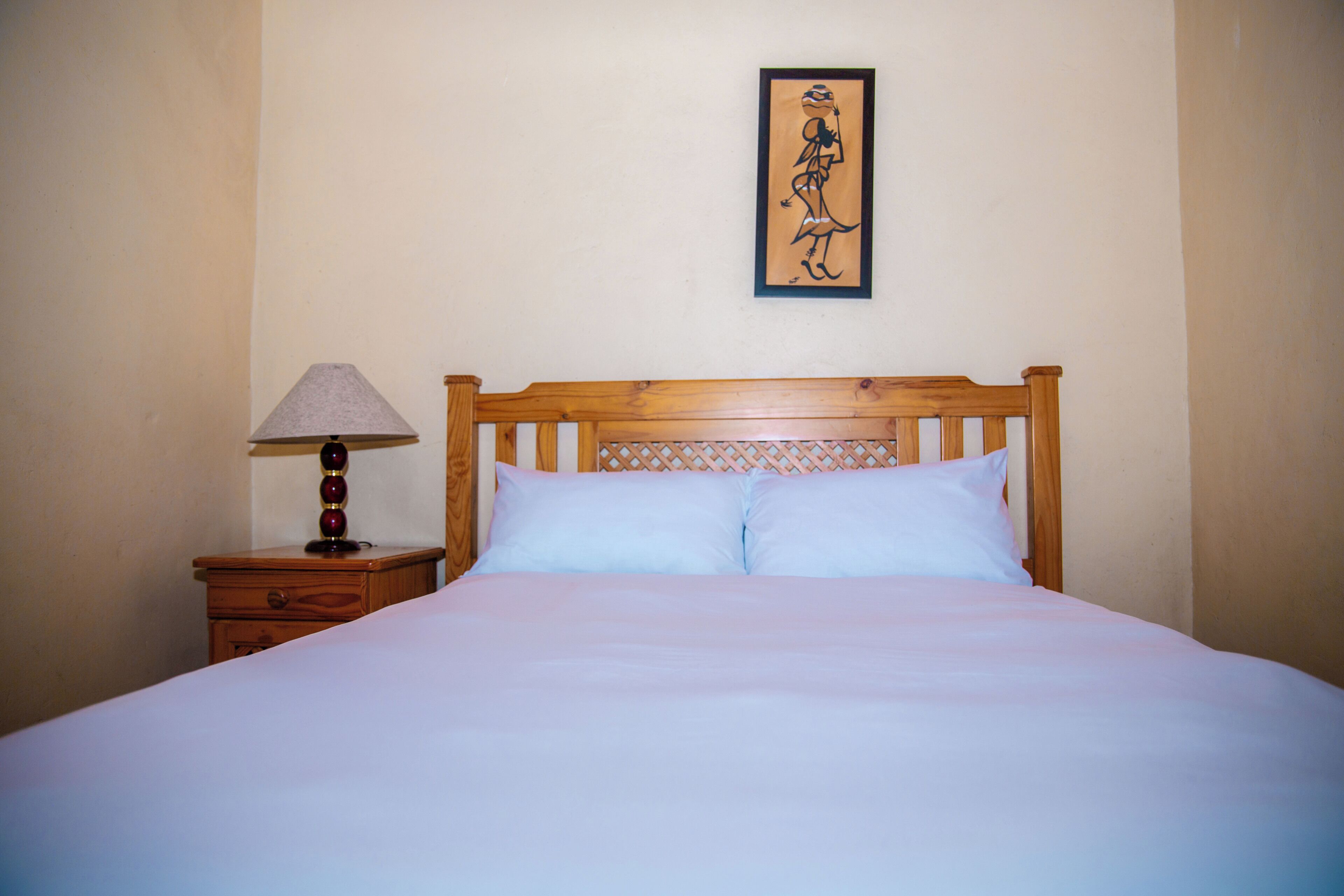 A neatly made bed with a wooden headboard, a bedside table with a lamp, and a framed picture on the wall.