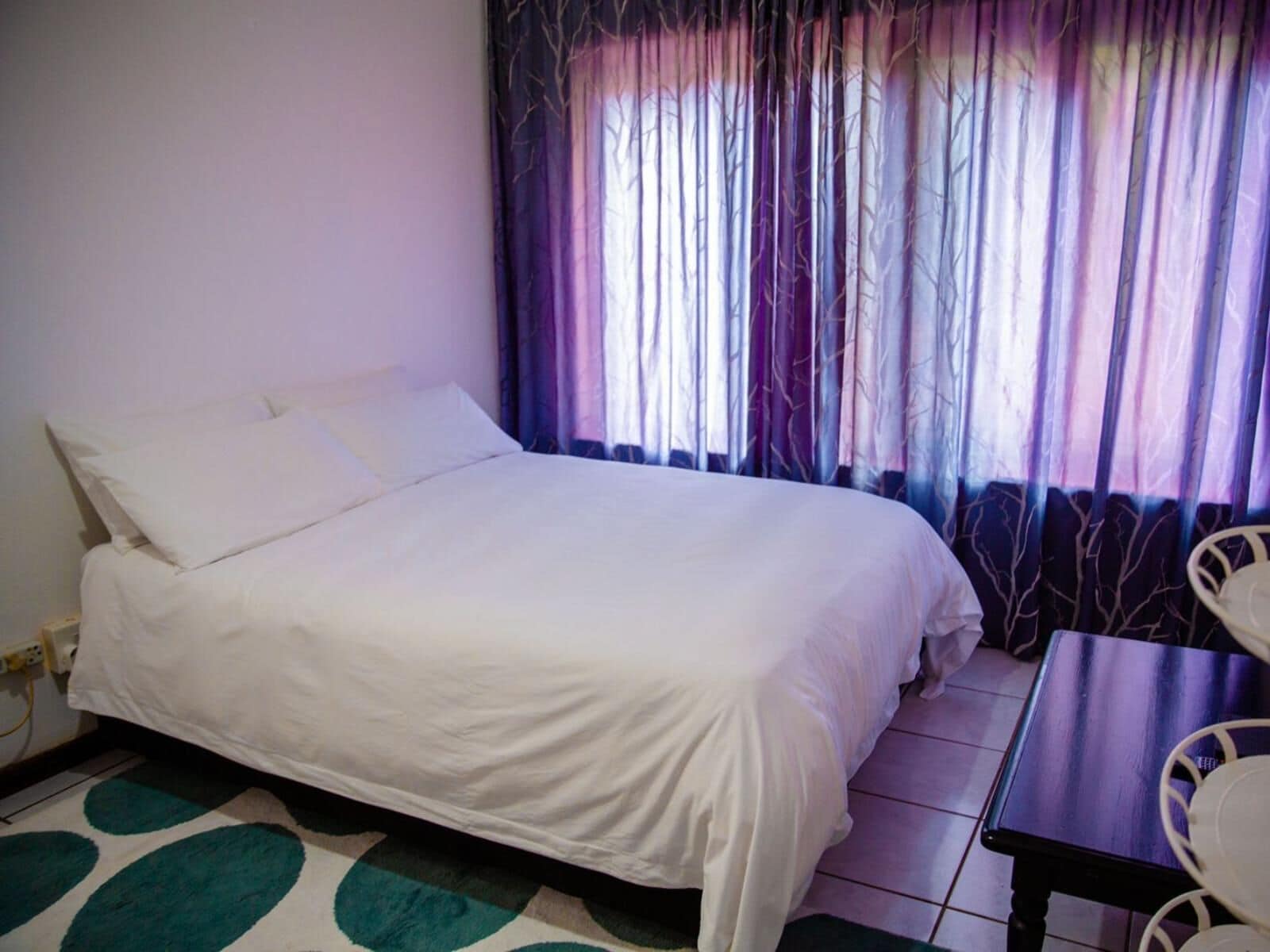 A single-bed room with a white bedspread, a small table, and a chair.