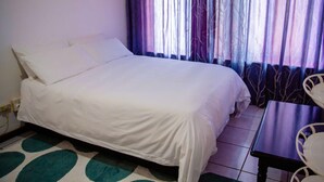 Habitación individual con una cama blanca, una mesita y una silla.
