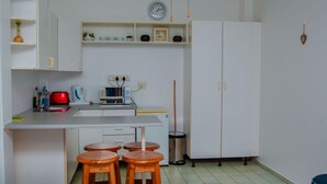 Cocina compacta con microondas, hervidor de agua y un reloj en la pared. Hay taburetes en la barra y un cubo de basura.