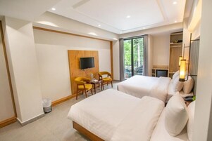 A hotel room with two beds, a TV, a small table with chairs, and a balcony with a view.