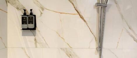 A bathroom with a marble wall, a handheld showerhead, and two soap dispensers.