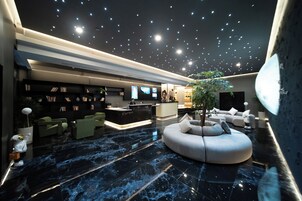 Um lobby moderno com teto estrelado, balcão de recepção, área de estar e uma grande árvore.