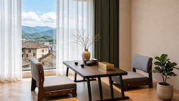 Una habitación con una mesa de madera, dos sillas, un florero con ramas, una planta en maceta y vistas a las montañas a través de una ventana.