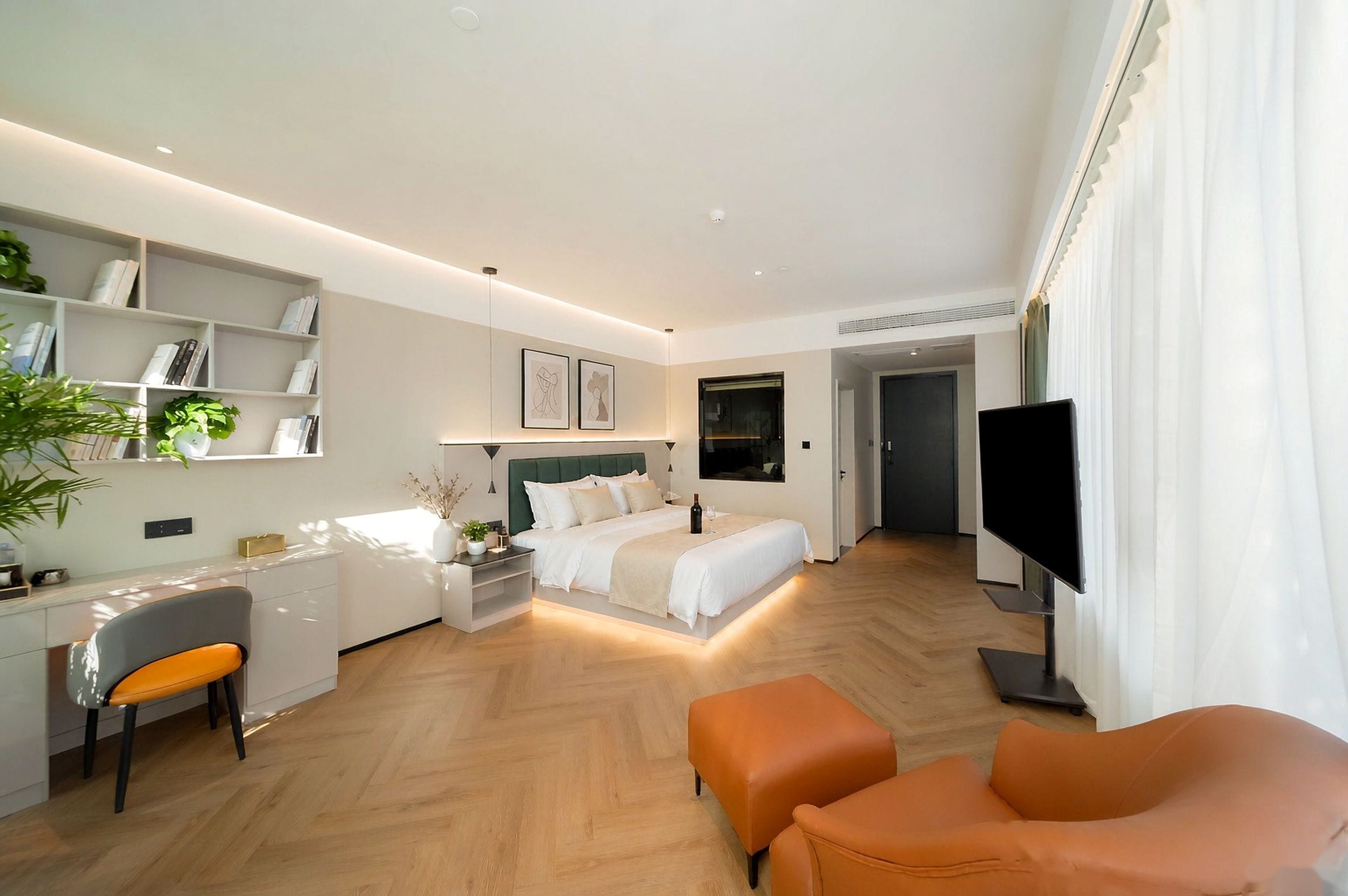 Quarto de hotel moderno com cama, escrivaninha, cadeira, televisão e uma pequena área de estar.