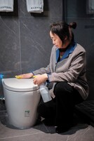 Una persona limpiando un inodoro con un atomizador y un paño.