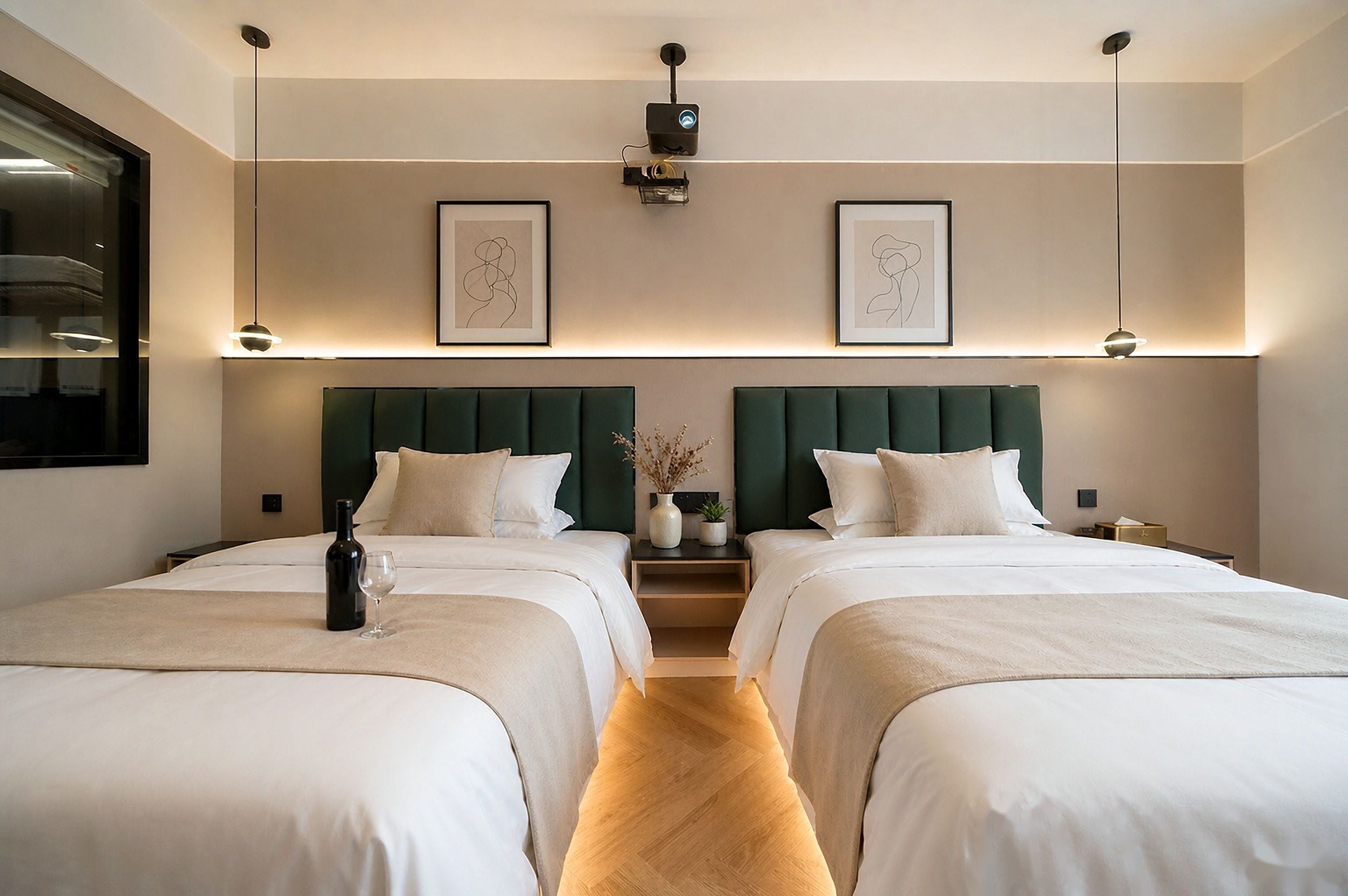 Habitación de hotel con dos camas, una mesita de noche con una botella y un vaso, un florero con plantas y una obra de arte en la pared.