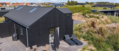 A modern black building with a wooden deck, outdoor seating, and a view of the surrounding landscape.