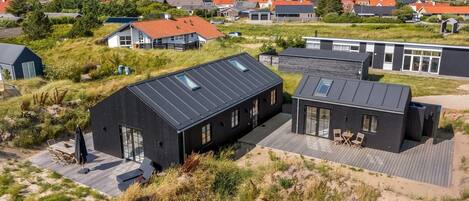 Ett modernt bostadsområde med hus som har platta tak och stora fönster, omgivet av vacker natur och med utsikt över havet.