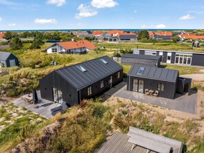 Ein modernes Wohngebiet mit Häusern, die flache Dächer und große Fenster haben, umgeben von Naturlandschaften und Blick auf das Meer.