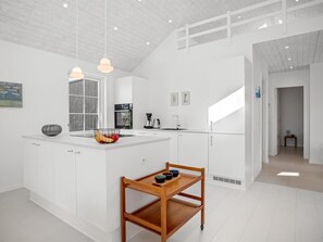 Eine moderne Küche mit weißen Schränken, einer zentralen Kochinsel, Pendelleuchten und einem Essbereich mit Holztisch und -stühlen.