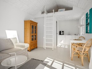 Un salon moderne comprenant un canapé, un meuble en bois, une table basse blanche et un coin repas avec des chaises en osier.