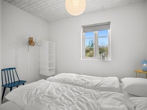 Ein Schlafzimmer mit zwei Betten, einem Sessel, einem Nachttisch mit Lampe, einem Fenster mit Blick auf Grünflächen und einer Hängeleuchte.