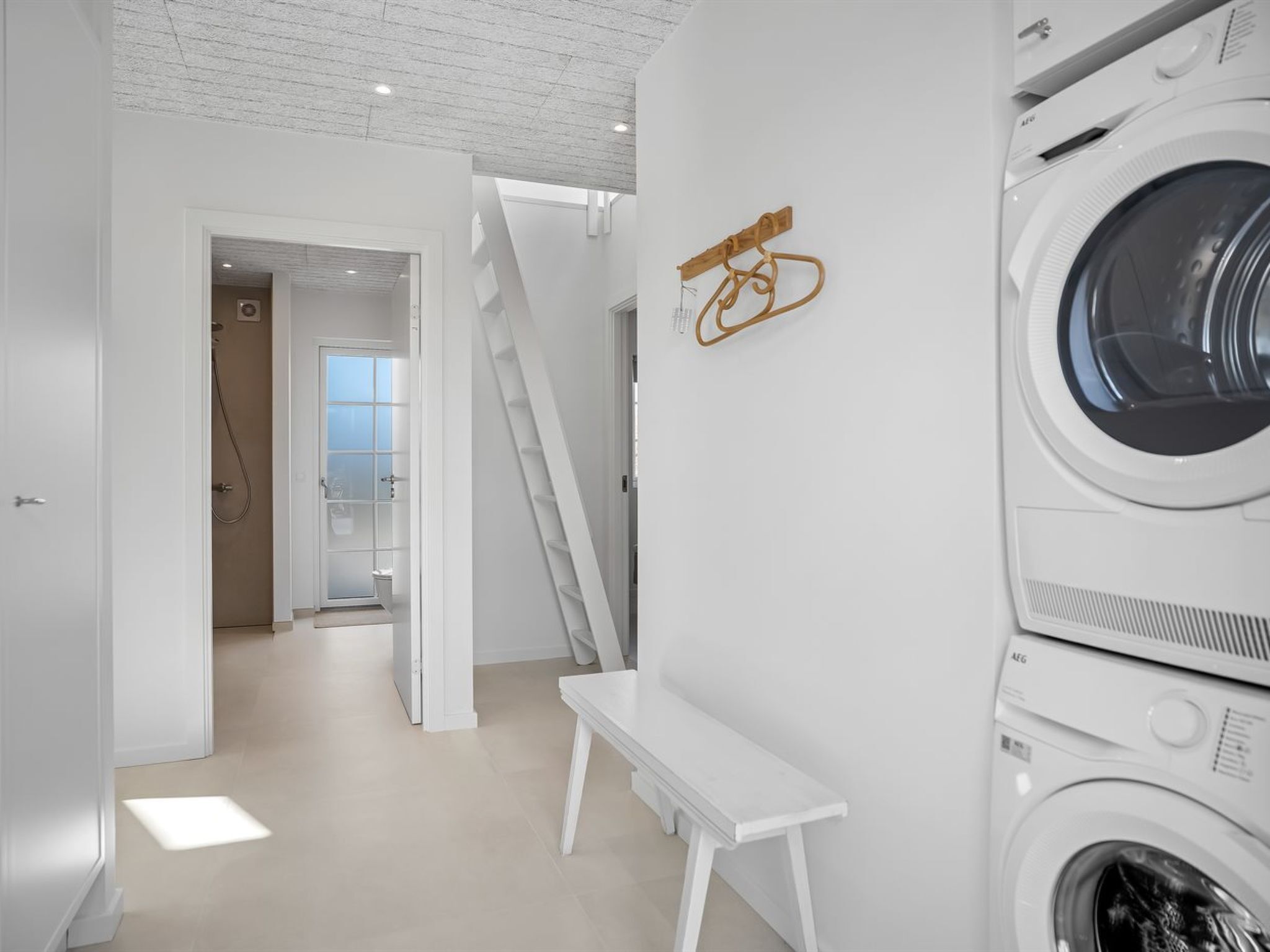 A laundry room with stacked washing machines, a bench, and a wooden art piece on the wall.