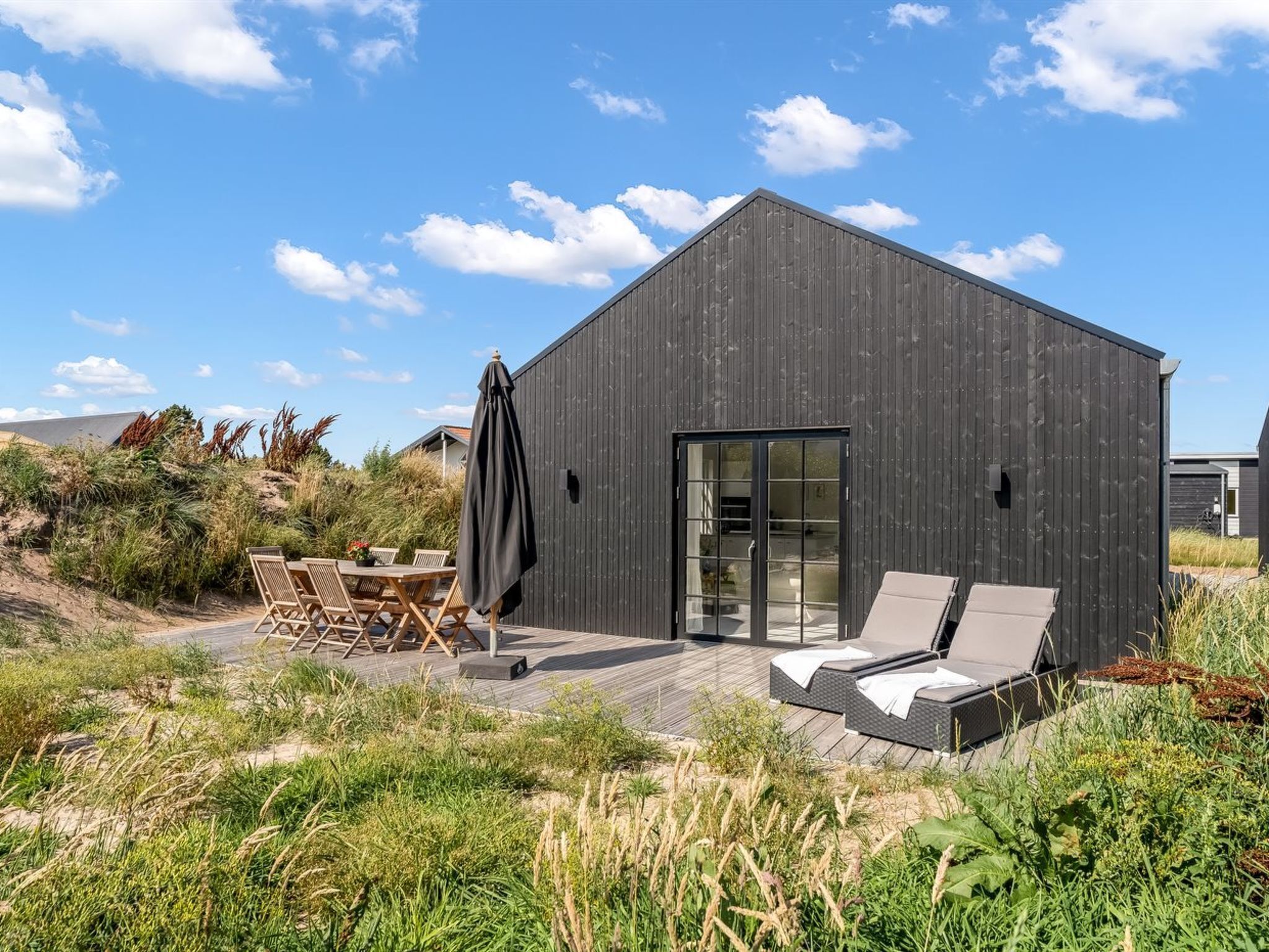 Un bâtiment moderne doté d’une grande porte vitrée, d’un espace extérieur aménagé pour s’asseoir et d’un patio.