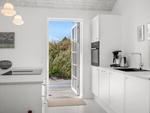 A modern kitchen with white cabinets, a built-in oven, a coffee maker, and a view of the outdoors. - "Selvi" - 500m from the sea by Interhome (Thisted)