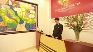 Un comptoir d’accueil d’hôtel agrémenté d’un grand tableau floral, un bureau de réception et une enseigne rouge portant le nom de l’hôtel.