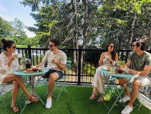 Quatre personnes sont assises à des tables rondes à l’extérieur, avec de l’herbe verte et des arbres en arrière-plan.