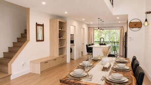 A dining area with a long wooden table set for six, a staircase, and a view of the outdoors. - Chic 2-story condo, a nature retreat for 6 (Québec City)