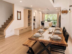 A dining area with a long wooden table set for six, a staircase, and a view of the outdoors. - Chic 2-story condo, a nature retreat for 6 (Québec City)