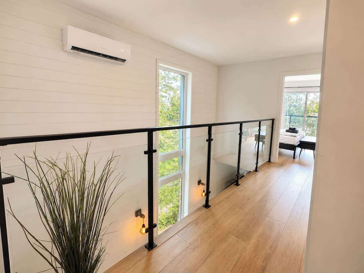A modern interior with a wooden floor, a glass railing, and a view of greenery outside.