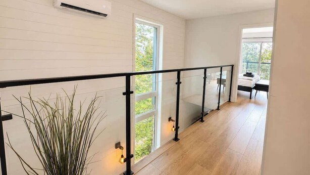 A modern interior with a wooden floor, a glass railing, and a view of greenery outside. - Chic 2-story condo, a nature retreat for 6 (Québec City)