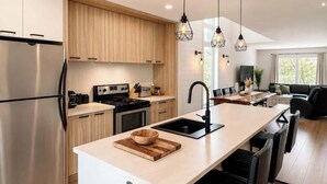 A modern kitchen with a central island, stainless steel appliances, and pendant lighting. - Chic 2-story condo, a nature retreat for 6 (Québec City)