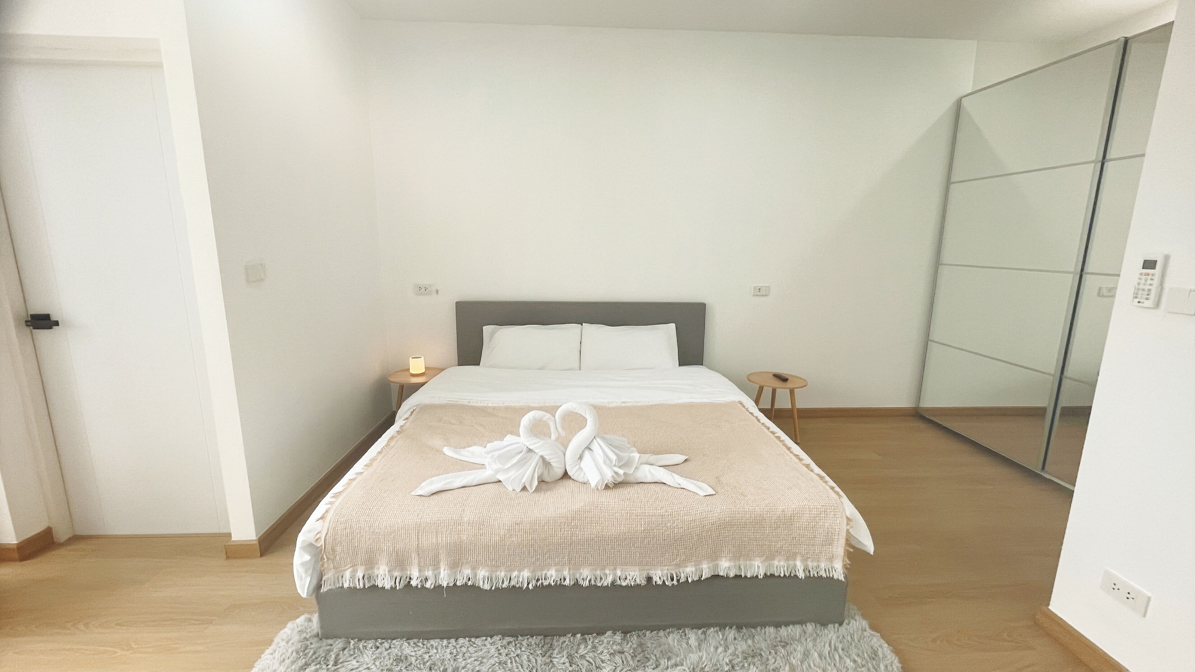 A hotel room with a bed, bedside tables, a mirror, and a fluffy rug.
