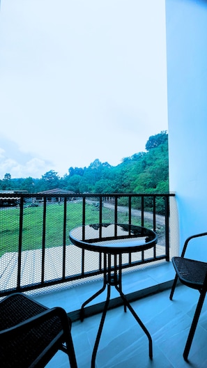 A balcony with a round table and two chairs, overlooking a green landscape. - Villa Risa (ราไวย์)