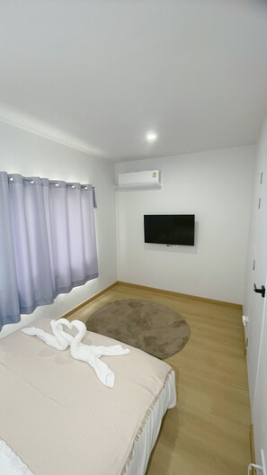 Une chambre à coucher comprenant un lit, un téléviseur à écran plat fixé au mur, un appareil de climatisation et une fenêtre avec des rideaux.