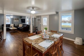 Un comedor con una mesa dispuesta para cuatro, una sala de estar con sofá y televisor, y un ventanal con vistas.