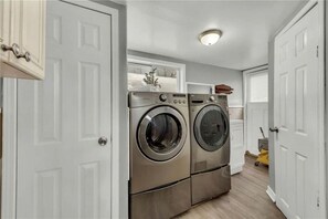 A laundry room with two stainless steel front-loading washers and dryers, a white door, and a ceiling light fixture.