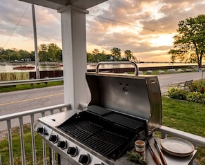 An outdoor grill with a view of a lake and a road during sunset.