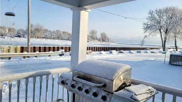 Un espace extérieur abrité, doté d’un barbecue recouvert de neige, d’une rambarde et offrant une vue sur un paysage enneigé.
