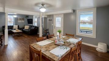 Ein Essbereich mit Tisch für vier Personen, ein Wohnzimmer mit Sofa und Fernseher sowie ein großes Fenster mit Blick.
