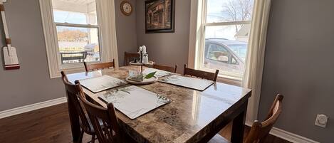 A dining room with a marble table, wooden chairs, and a view of the outside through large windows.