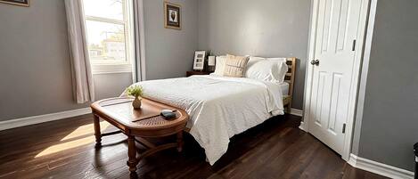 A bedroom with a bed, a bedside table, a window with curtains, and a door.