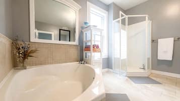 A bathroom with a large bathtub, a glass shower enclosure, and a mirror above the tub.