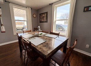 A dining room with a marble table, wooden chairs, and a view of the outside through large windows.