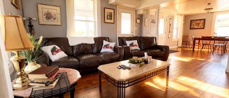 A spacious living room with a brown leather sofa set, a coffee table, and a dining area with a wooden table and chairs.