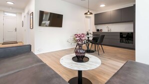 Un soggiorno moderno con un tavolo rotondo in marmo, un vaso con fiori, un divano, un'area da pranzo con sedie e una cucina con mobili grigi.