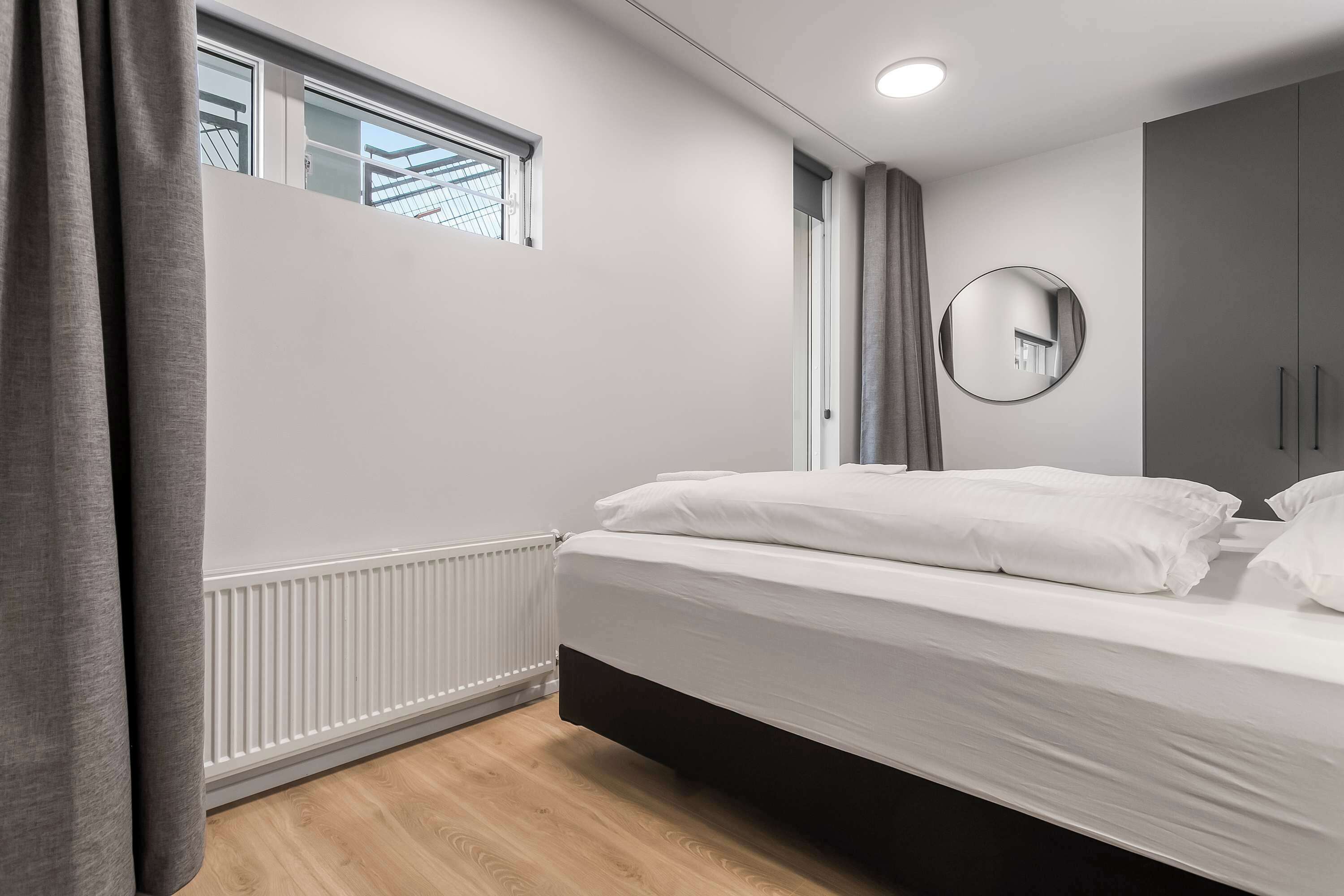 A bedroom with a bed, a window, a mirror, and a wardrobe.