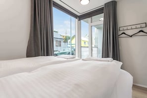 Une chambre d’hôtel avec deux lits, une fenêtre avec des rideaux, une vue sur la rue et un porte-manteau avec des cintres.