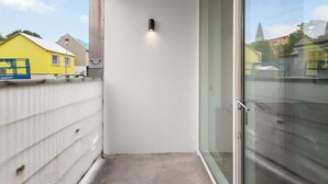Un balcone stretto con una porta in vetro, un muro bianco e un piccolo fiorino.