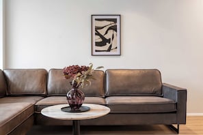 A brown leather sofa, a round table with a vase of flowers, and a framed abstract painting on the wall. - Njálsgata Apartments by Heimaleiga (Reykjavík)