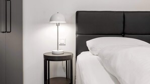 Una moderna camera d'albergo con un letto, un comodino con una lampada e un armadio.