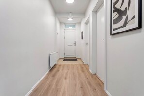 Un couloir avec un plancher en bois, des murs blancs et une porte au fond.