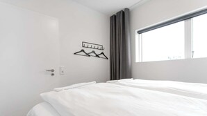 Een hotelkamer met twee bedden, een raam met gordijnen en een kapstok aan de muur.