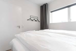 Ein Hotelzimmer mit zwei Betten, einem fensterbelaubten Fenster und einem Wandhaken für Kleidung.